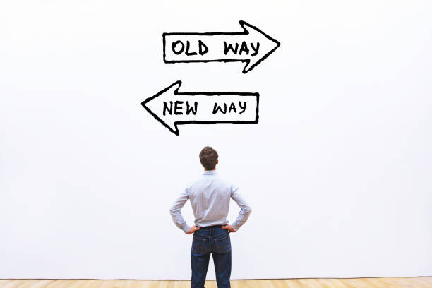 Man staat voor een witte muur waar twee pijlen op zijn getekend. Er gaat een pijl naar links war "new way" op staat en de pijl naar rechts staat "old way" op. Het staat symbool voor de strategie die bedrijven moeten kiezen.