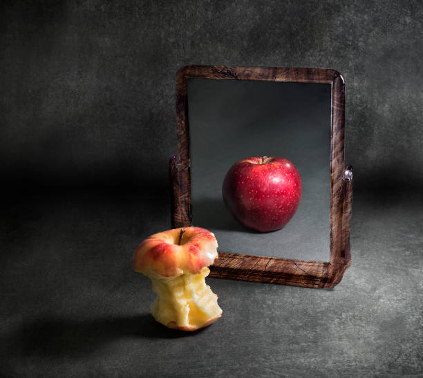 Appel met een vervormde reflectie in een spiegel tegen een grijze achtergrond, als symbool voor eetgedrag en voeding, zelfbeeld en lichaamsbeleving.