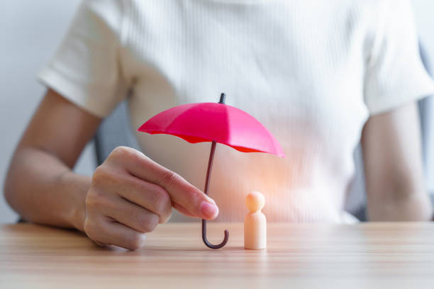 Conceptbeeld van begeleiding, bescherming en duurzame groei. Hand die een houten figuur beschermt met een rode paraplu.