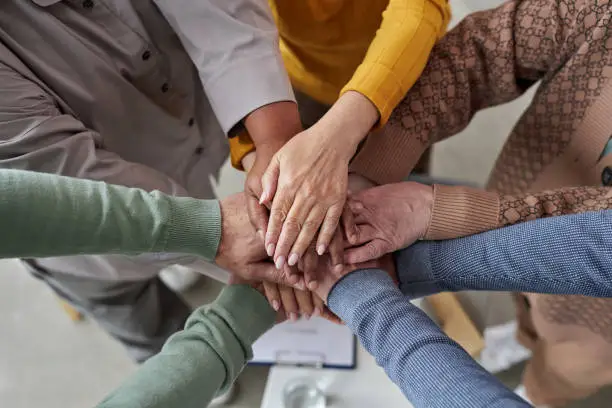 Groep mensen die hun handen op elkaar legt als symbool voor verbinding, samenwerking en ondersteuning van ouderen.