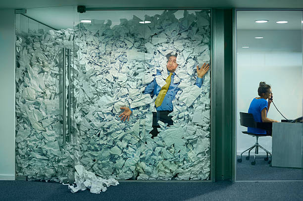 Zakenman vast in een glazen kantoor door een overvloed aan papieren ideeën als symbool voor burn-out & herstel preventie, werkdruk en efficiënter werken.